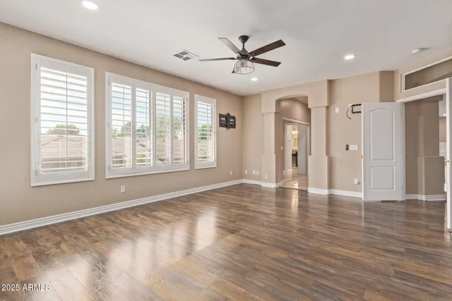 a view of an empty room with wooden floor and a ceiling fan