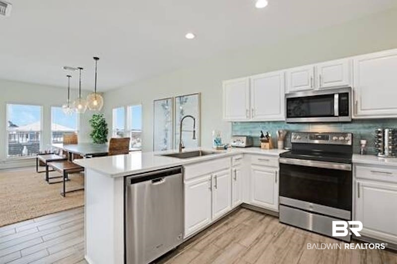 1492 Shell Lane Gulf Shores, AL 36542 - Photo 6 of 20 Kitchen featuring stainless steel appliances, light wood-style flooring, a peninsula, backsplash, and white cabinets