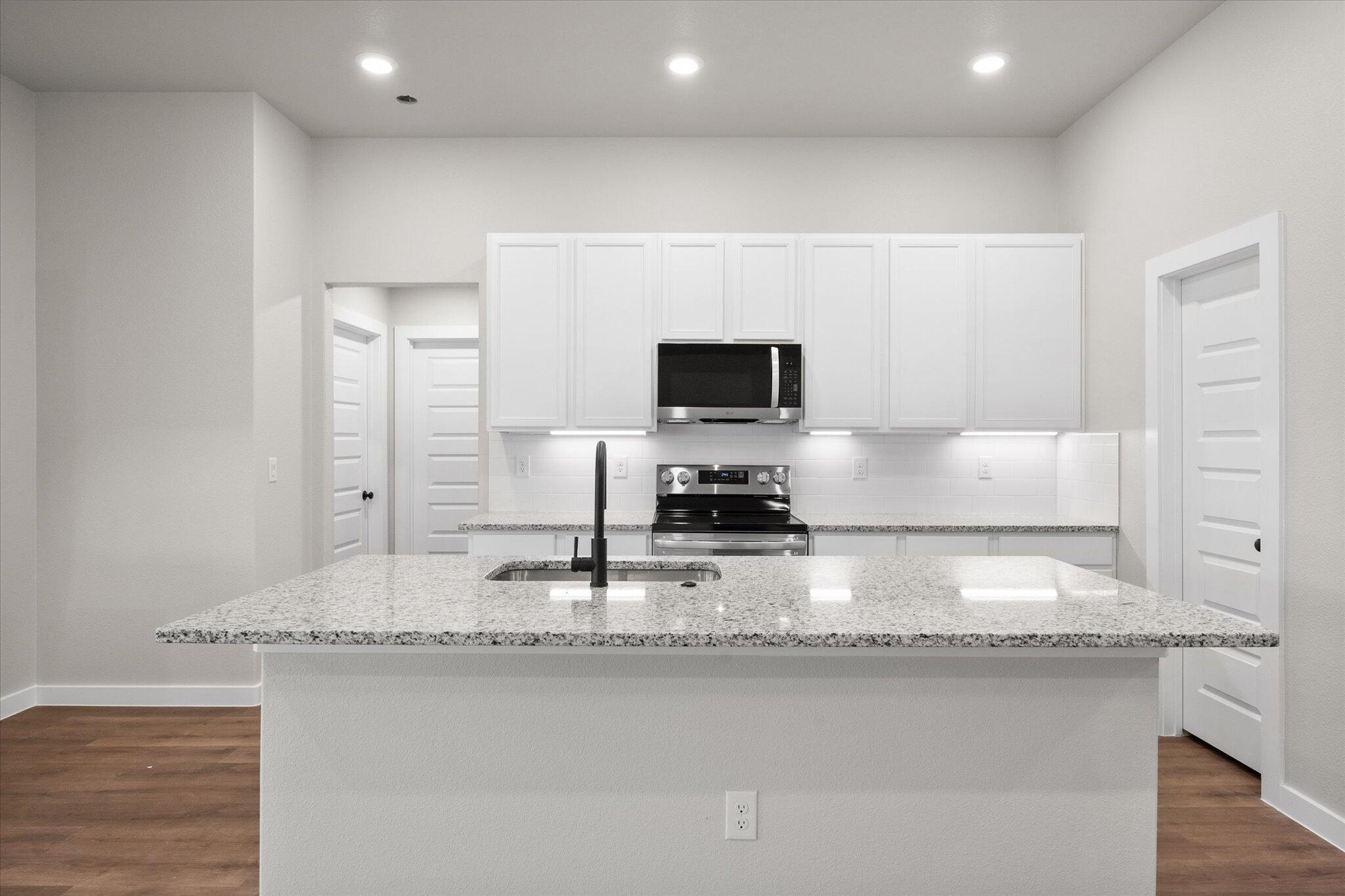 3022 140th Street Lubbock, TX 79423 - Photo 8 of 20 a kitchen with granite countertop a sink a stove a microwave a refrigerator and white cabinets with wooden floor