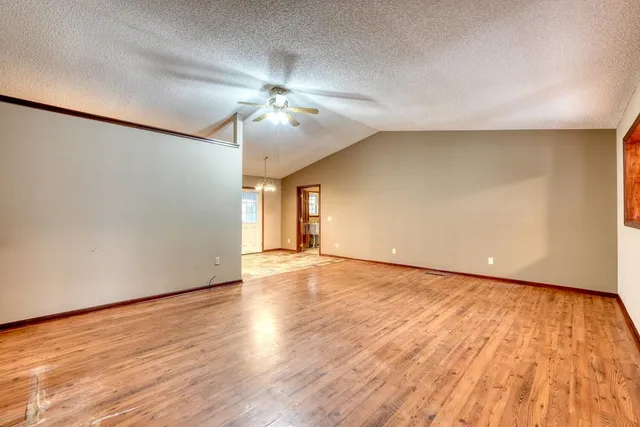 a view of an empty room with wooden floor and a ceiling fan