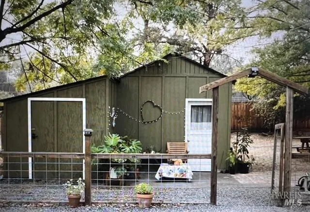 a small barn in front of a yard with plants and large trees