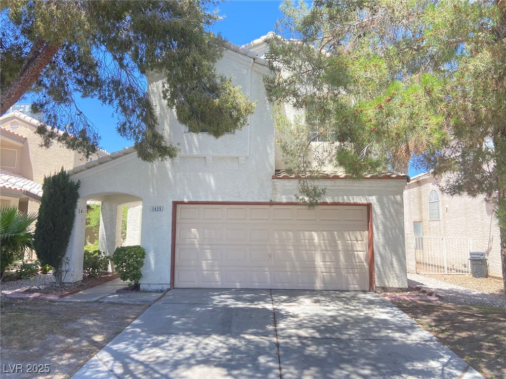 View of front of house with a tiled roof, stucco siding, driveway, and an attached garage