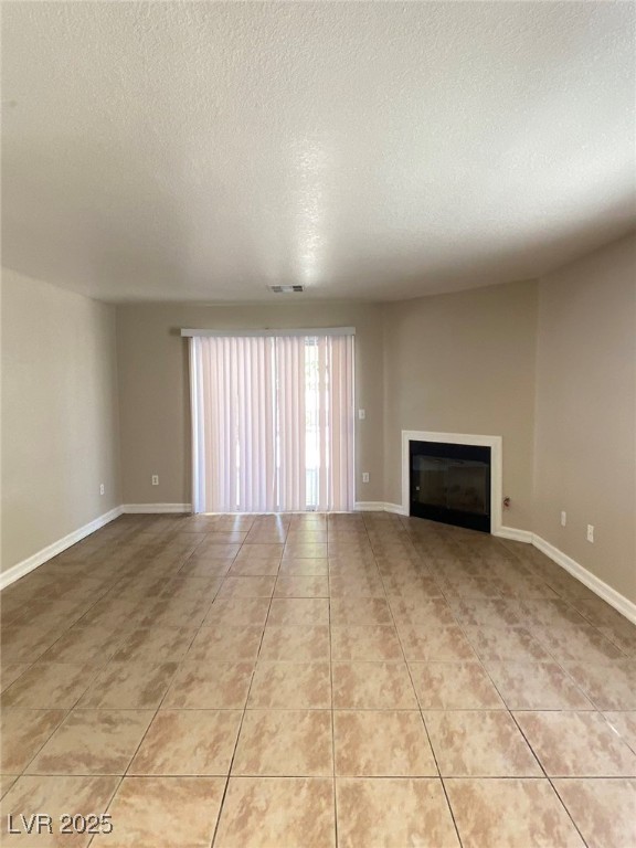 1425 Spice Sky Drive Las Vegas, NV 89128 - Photo 5 of 16 Unfurnished living room featuring a textured ceiling, light tile patterned floors, and a glass covered fireplace