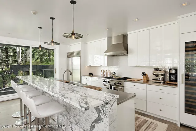 a kitchen with stainless steel appliances granite countertop a stove a sink a refrigerator wooden floor and a large window