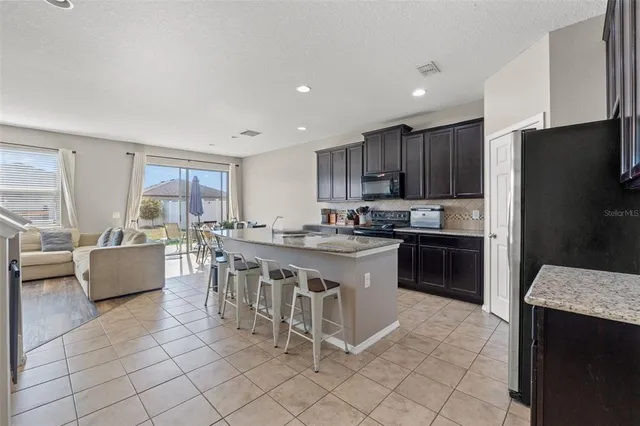 a kitchen with stainless steel appliances granite countertop a refrigerator a stove a sink a dining table and chairs