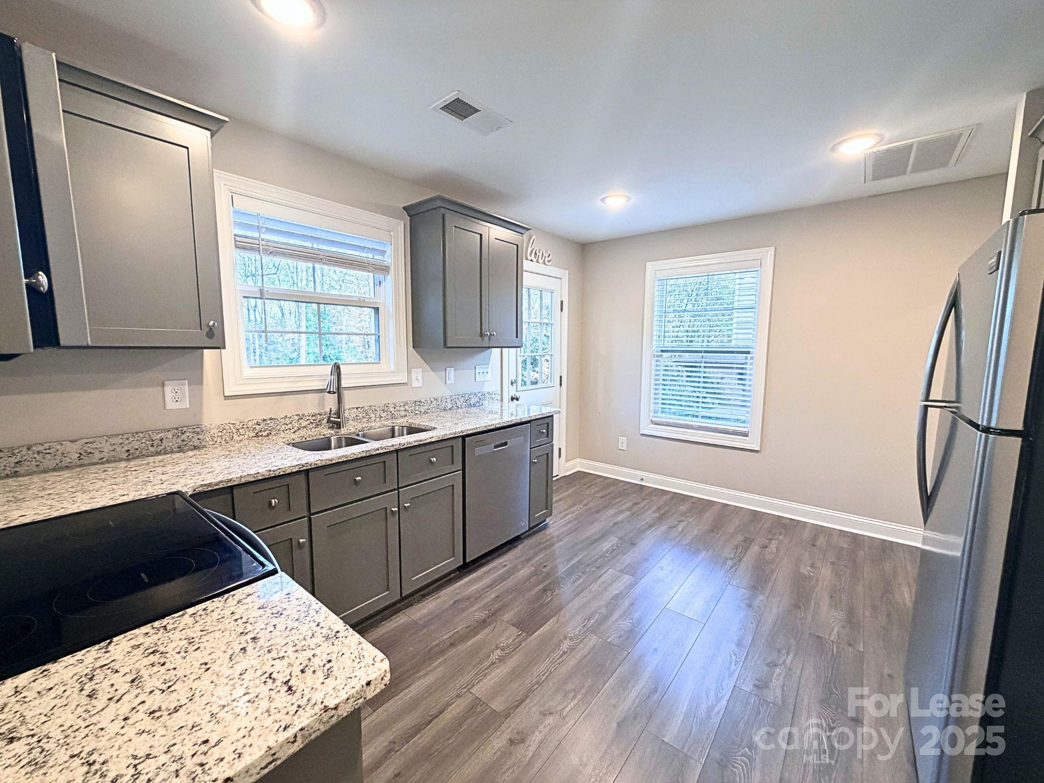 921 Pineridge Street Southeast Concord, NC 28025 - Photo 3 of 13 a kitchen with stainless steel appliances kitchen island granite countertop wooden floors wooden cabinets a sink and a window