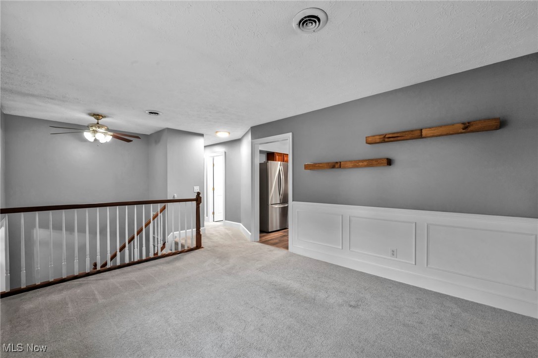 47655 Cooper Foster Park Road Amherst, OH 44001 - Photo 5 of 49 Empty room featuring a decorative wall, carpet, a wainscoted wall, a textured ceiling, and ceiling fan