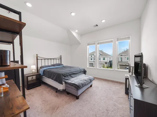 a spacious bedroom with a bed and a flat tv screen on the dresser