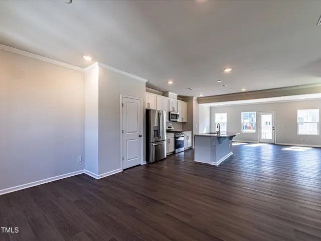 a view of an empty room with wooden floor and a kitchen