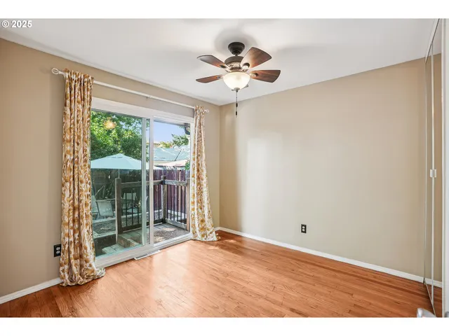 a view of an empty room with wooden floor and fan