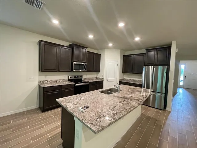 a kitchen with kitchen island granite countertop wooden cabinets refrigerator and microwave