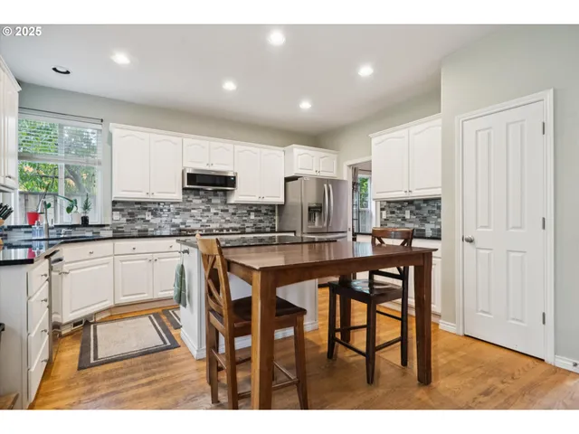 a kitchen with stainless steel appliances granite countertop a stove a sink a microwave a refrigerator and white cabinets with wooden floor