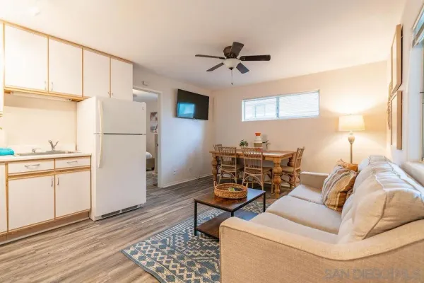 a living room with furniture a white refrigerator and kitchen view
