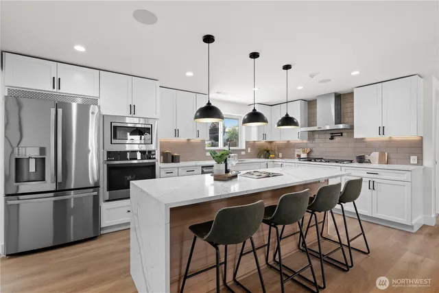 a view of a kitchen with kitchen island stainless steel appliances a table chairs sink and wooden floor