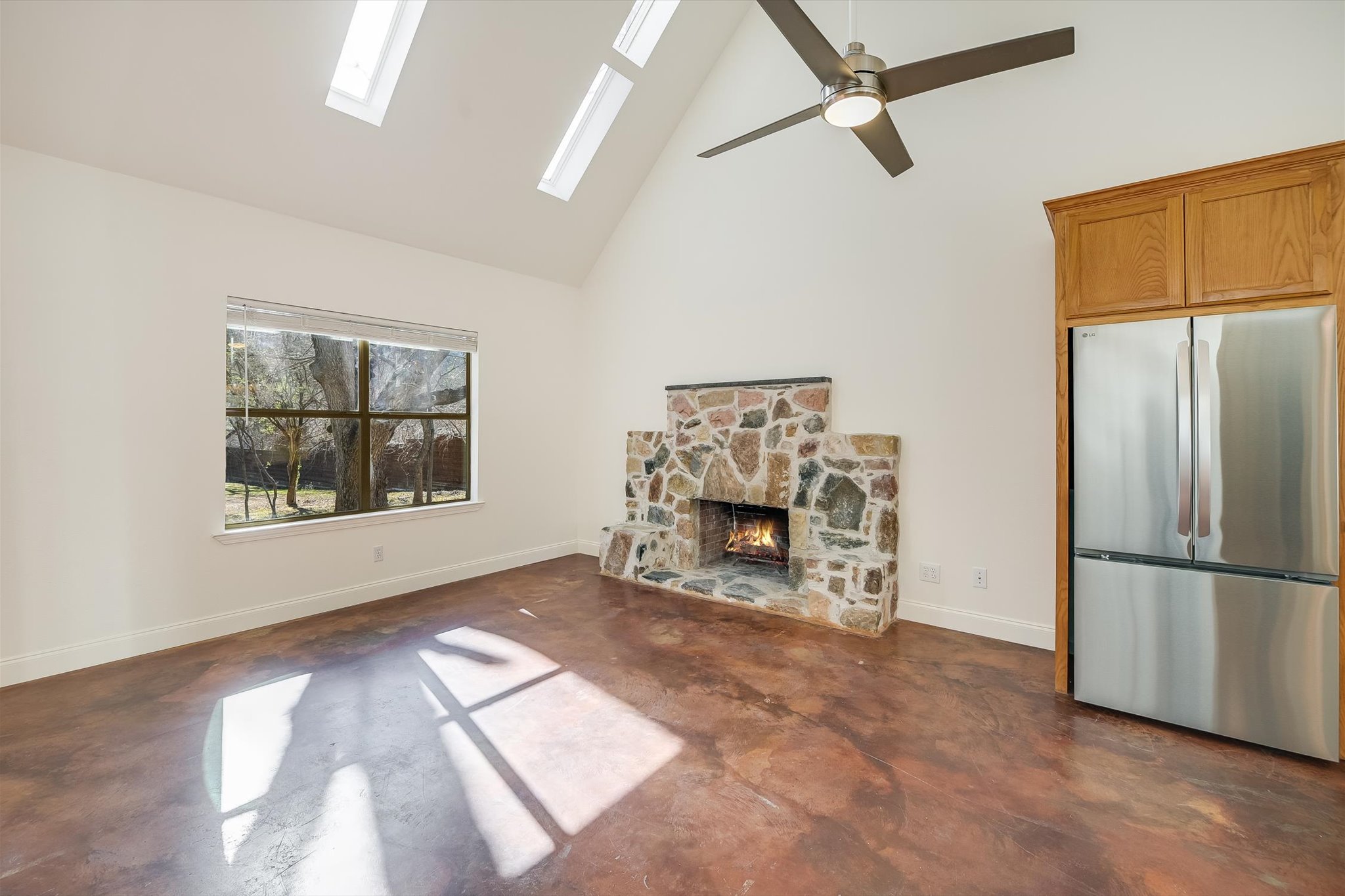 302 Lago Verde Road Lakeway, TX 78734 - Photo 4 of 21 Unfurnished living room featuring finished concrete floors, high vaulted ceiling, a fireplace, a skylight, and ceiling fan
