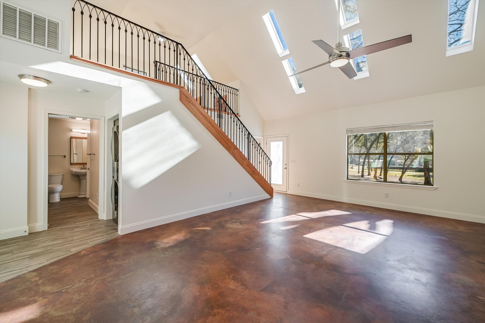 302 Lago Verde Road Lakeway, TX 78734 - Photo 7 of 21 Unfurnished living room featuring a towering ceiling, a skylight, concrete floors, stairs, and ceiling fan