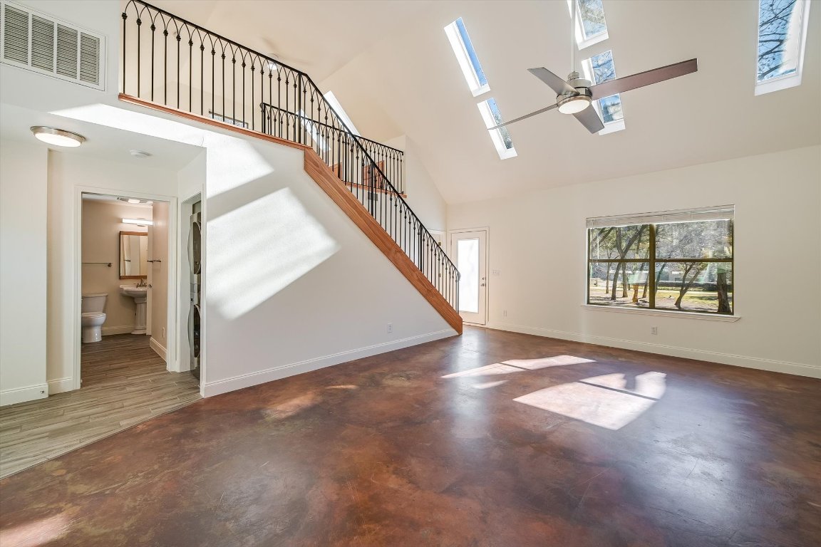 302 Lago Verde Road Lakeway, TX 78734 - Photo 7 of 21 Unfurnished living room featuring a towering ceiling, a skylight, concrete floors, stairs, and ceiling fan