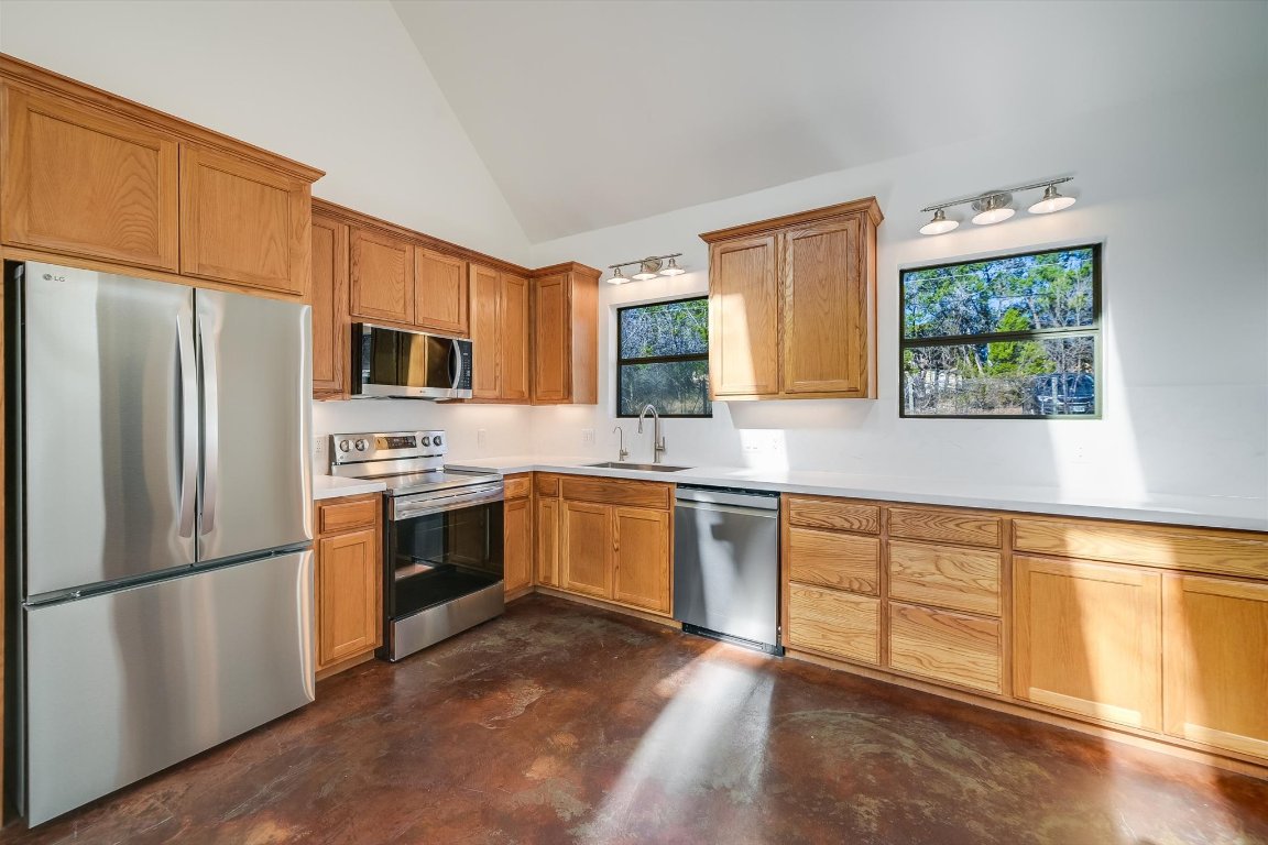 302 Lago Verde Road Lakeway, TX 78734 - Photo 8 of 21 Kitchen featuring appliances with stainless steel finishes, light countertops, concrete floors, high vaulted ceiling, and brown cabinets