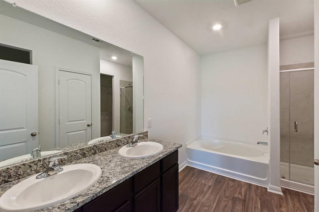 16429 Farmhouse Lane Elgin, TX 78621 - Photo 10 of 22 Bathroom with a dual vanity featuring a speckled countertop and undermount sinks, a built-in bathtub, a walk-in shower with a glass enclosure, and wood-finish flooring