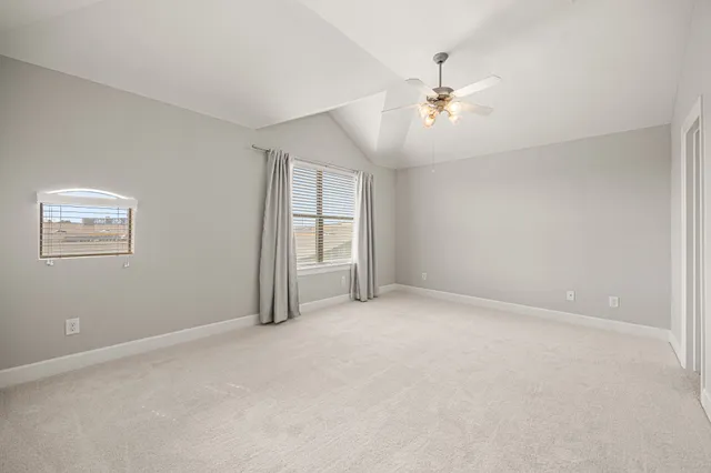 an empty room with chandelier fan and windows