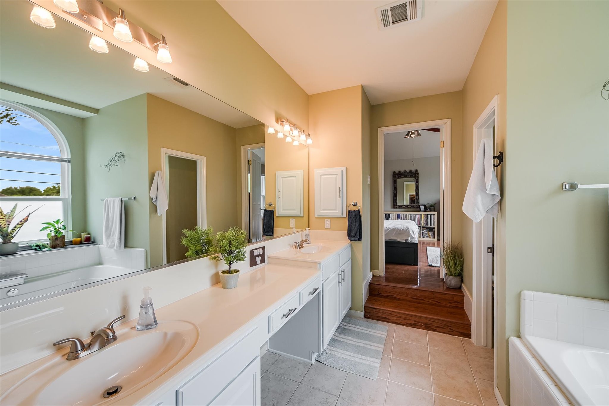 6456 Ruxton Lane Austin, TX 78749 - Photo 18 of 30 A well-lit primary bathroom featuring dual sinks, a large mirror, and a built-in tub with an arched window view.
