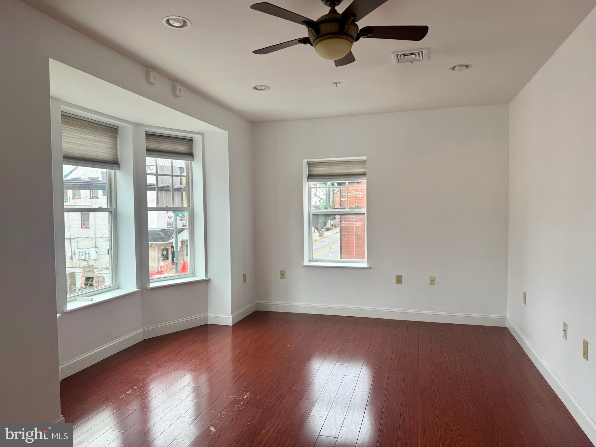 an empty room with wooden floor fan and windows