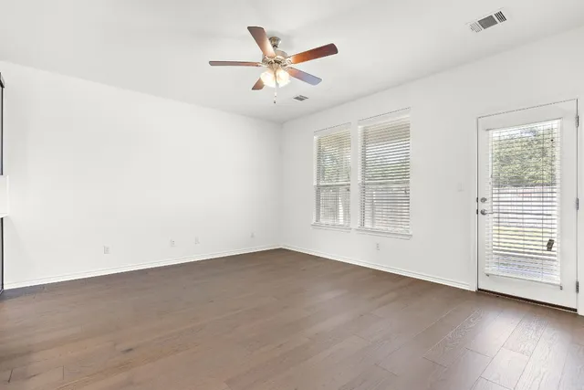 an empty room with wooden floor fan and windows