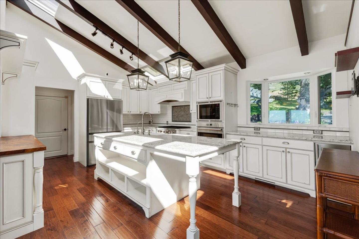 15 Mentone Road Carmel, CA 93923 - Photo 6 of 47 a large white kitchen with stainless steel appliances granite countertop a stove a sink dishwasher and a fireplace with wooden floor