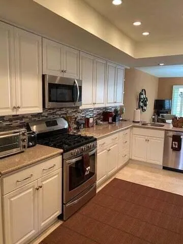 a white kitchen with granite countertop a stove top oven a sink dishwasher and cabinets with wooden floor