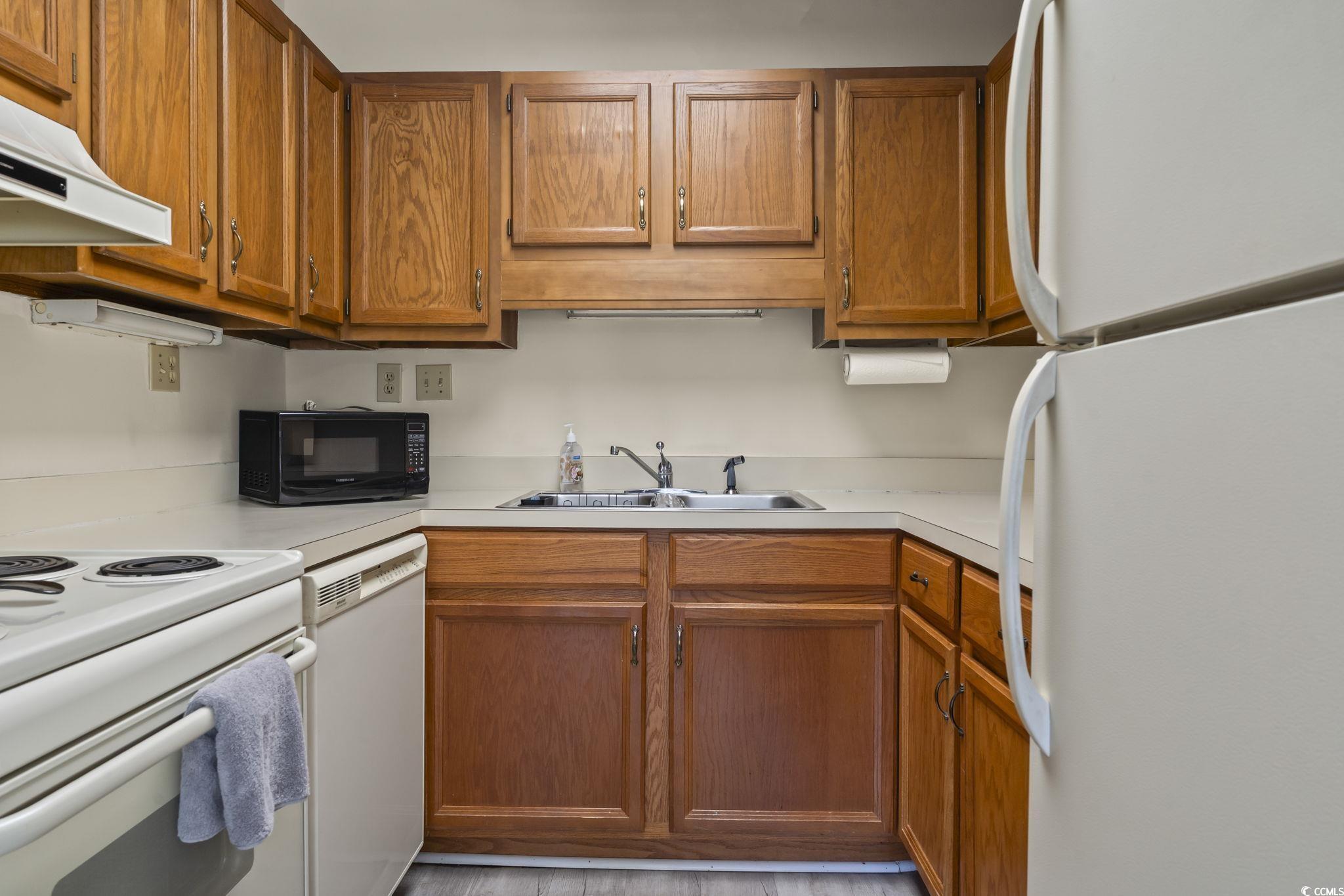 5001 Little River Road, Unit W106 Myrtle Beach, SC 29577 - Photo 7 of 28 Kitchen with white appliances, brown cabinets, and light countertops