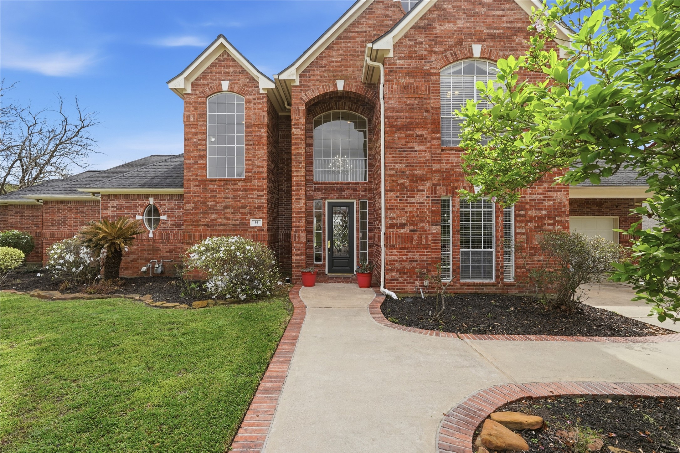 55 Monterrey Road East Montgomery, TX 77356 - Photo 1 of 50 This photo showcases a beautiful two-story brick home with large windows and a welcoming arched entryway. The well-maintained landscaping features shrubs and a lush lawn, creating an inviting curb appeal.