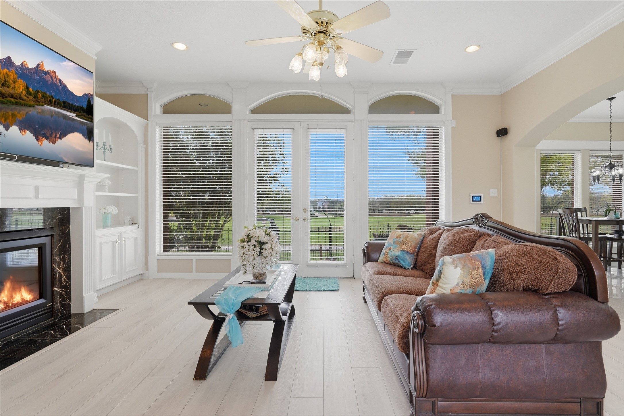 55 Monterrey Road East Montgomery, TX 77356 - Photo 12 of 50 Bright and inviting living room with large windows offering stunning views. Features a cozy fireplace, elegant ceiling fan, and stylish built-in shelving. Ideal for relaxation and entertaining.