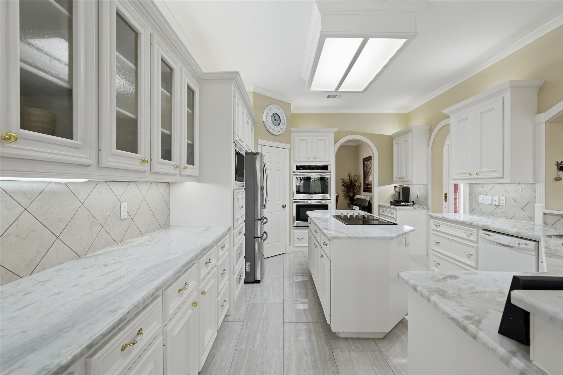 55 Monterrey Road East Montgomery, TX 77356 - Photo 15 of 50 This kitchen features elegant white cabinetry with glass-front doors, marble countertops, and a central island with a cooktop. It includes modern appliances, ample storage, and a tiled backsplash, creating a bright and spacious cooking area.