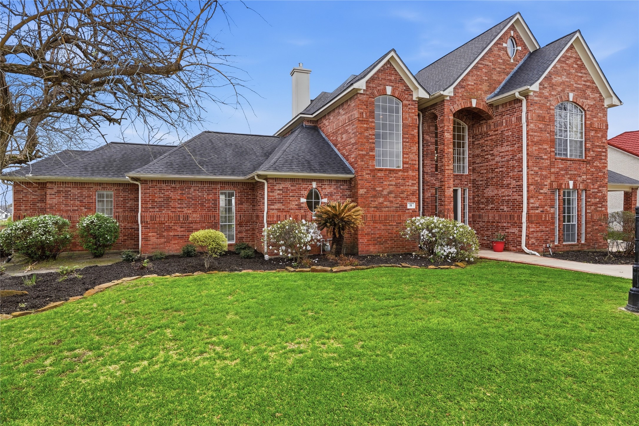 55 Monterrey Road East Montgomery, TX 77356 - Photo 2 of 50 This elegant two-story brick home features large arched windows, a well-maintained lawn, and landscaped garden beds, offering a charming curb appeal in a desirable neighborhood.