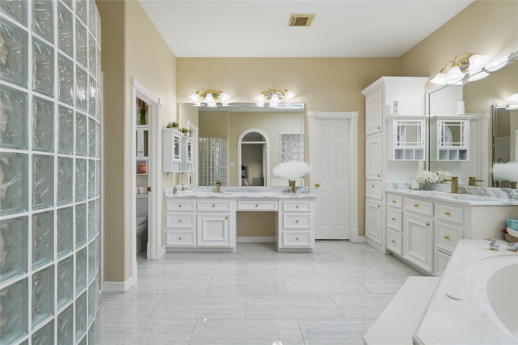 55 Monterrey Road East Montgomery, TX 77356 - Photo 24 of 50 This spacious bathroom features elegant tile flooring, dual vanities with ample storage, and a luxurious soaking tub. Glass block accents add a touch of modern design, complementing the bright and airy ambiance.