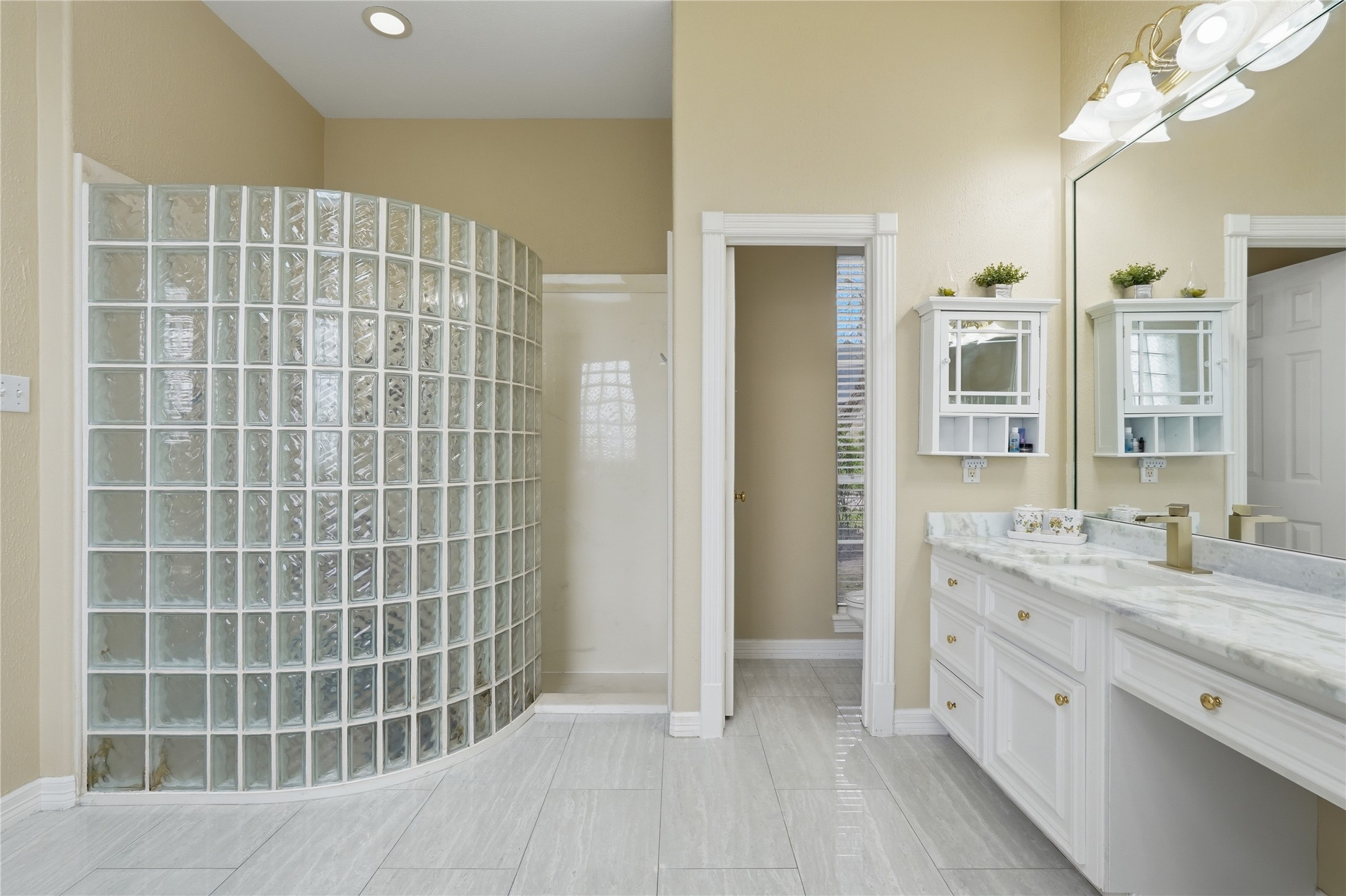 55 Monterrey Road East Montgomery, TX 77356 - Photo 25 of 50 This bathroom features a spacious layout with a curved glass block shower, dual sinks with marble countertops, and ample storage. The neutral color palette and large mirror enhance the bright, airy feel.