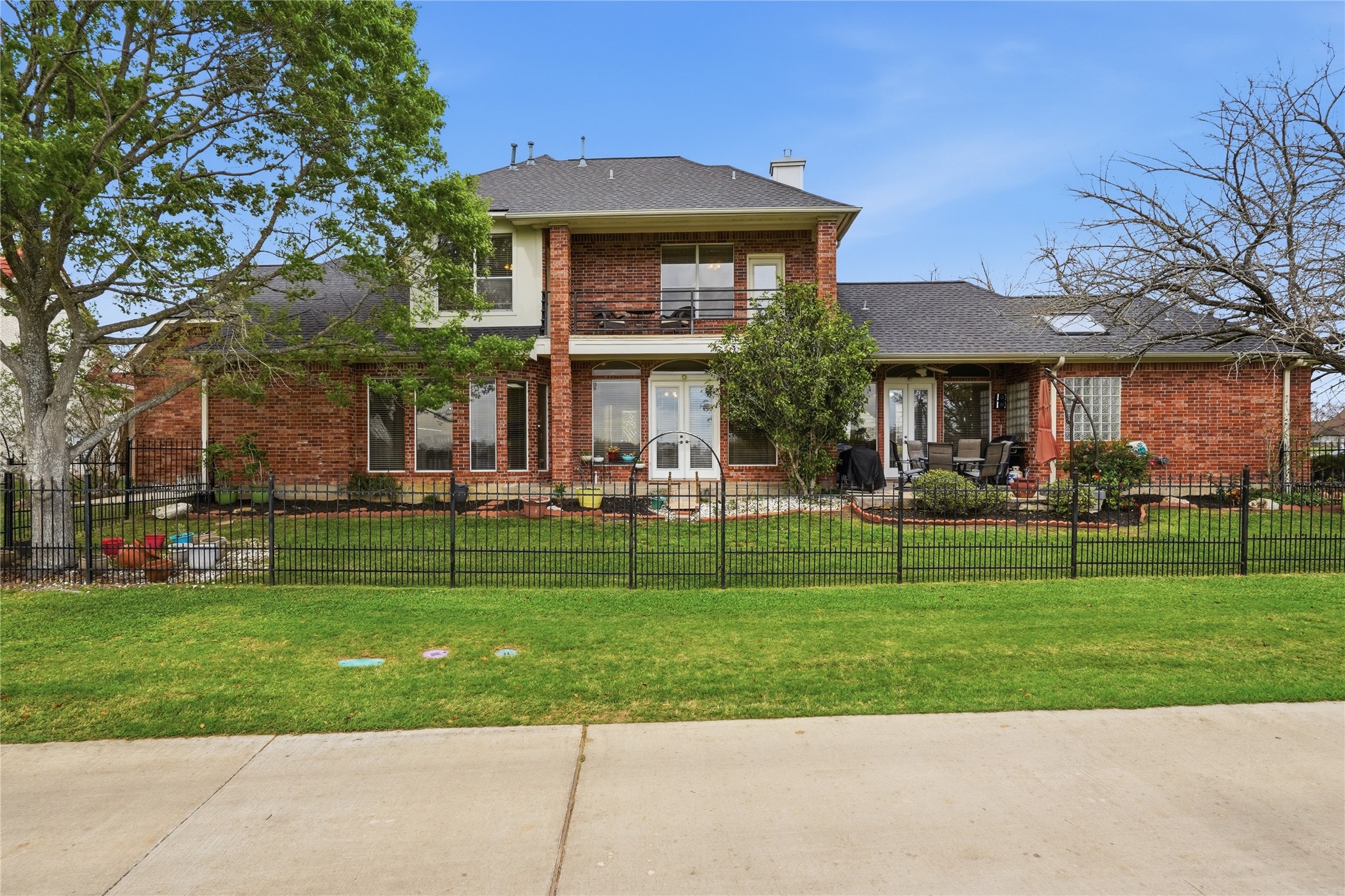 55 Monterrey Road East Montgomery, TX 77356 - Photo 41 of 50 This photo shows a spacious two-story brick home with a well-kept lawn and a fenced backyard. The house features large windows, a patio area with outdoor seating, and mature trees providing shade. Ideal for those seeking a blend of comfort and outdoor living.
