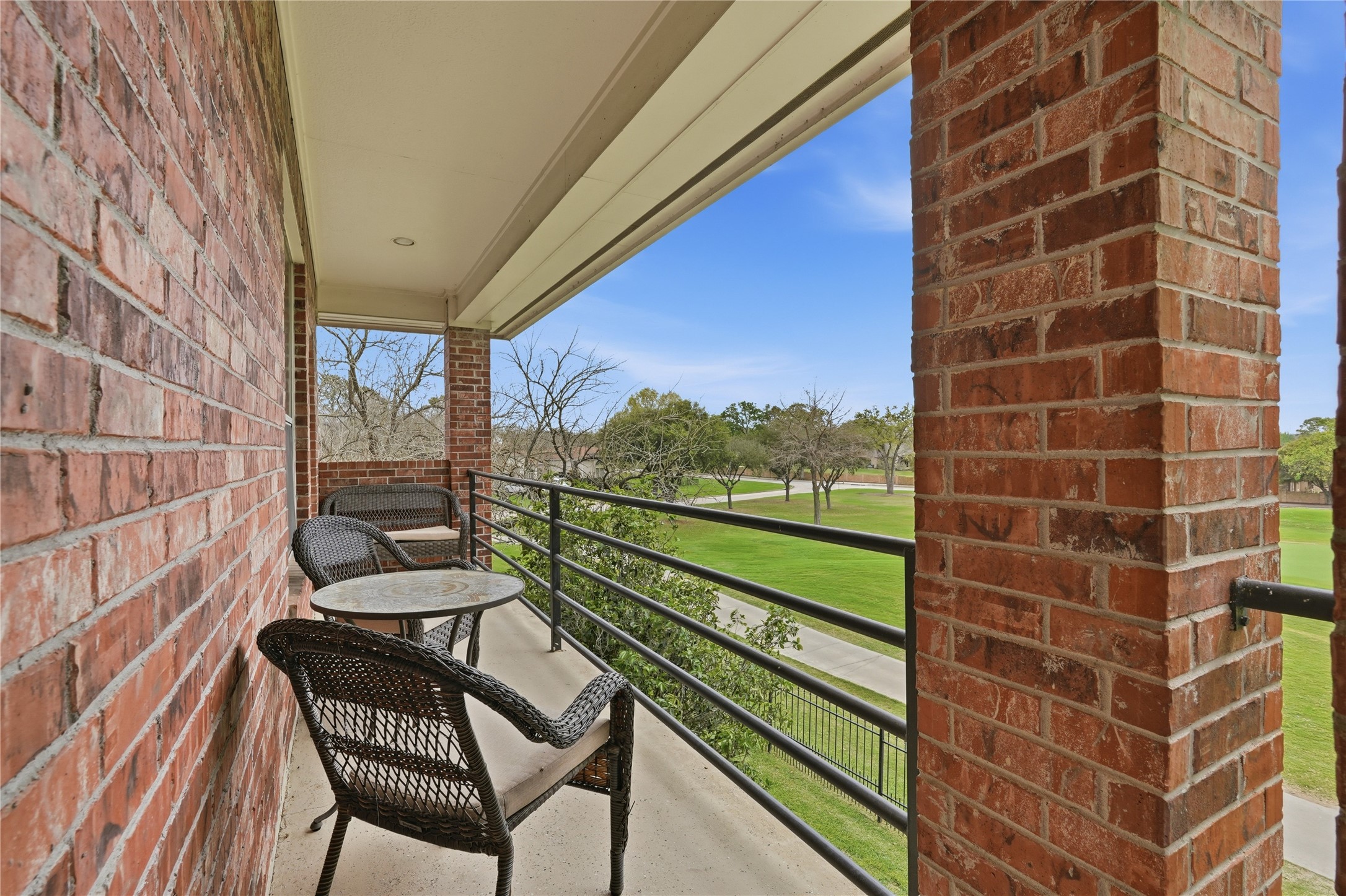 55 Monterrey Road East Montgomery, TX 77356 - Photo 42 of 50 This photo showcases a cozy balcony with brick walls, featuring a small table and chairs. It overlooks a lush green landscape, providing a serene outdoor space perfect for relaxation.