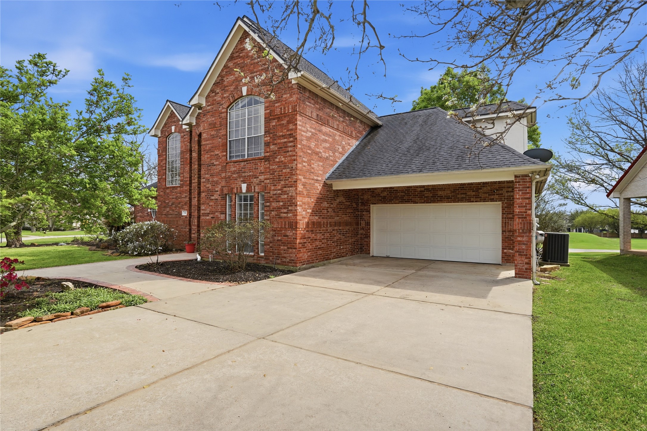 55 Monterrey Road East Montgomery, TX 77356 - Photo 5 of 50 This photo shows a two-story brick house with a spacious driveway leading to a two-car garage. The property features a well-maintained lawn and mature trees, offering a welcoming and attractive curb appeal.
