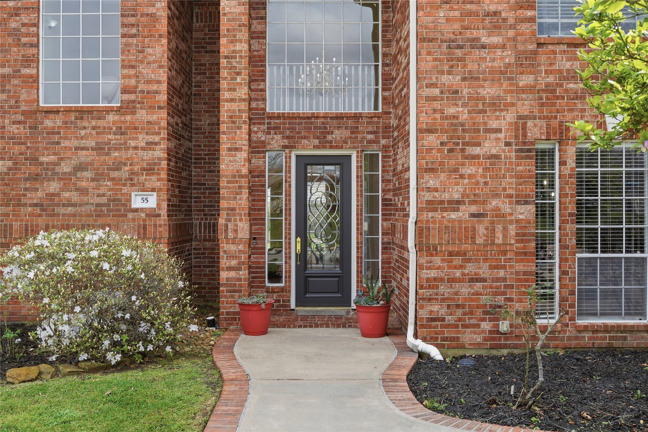 55 Monterrey Road East Montgomery, TX 77356 - Photo 6 of 50 Charming brick home entrance featuring a decorative glass front door, large windows for natural light, and a welcoming walkway framed by well-maintained shrubs and planters.