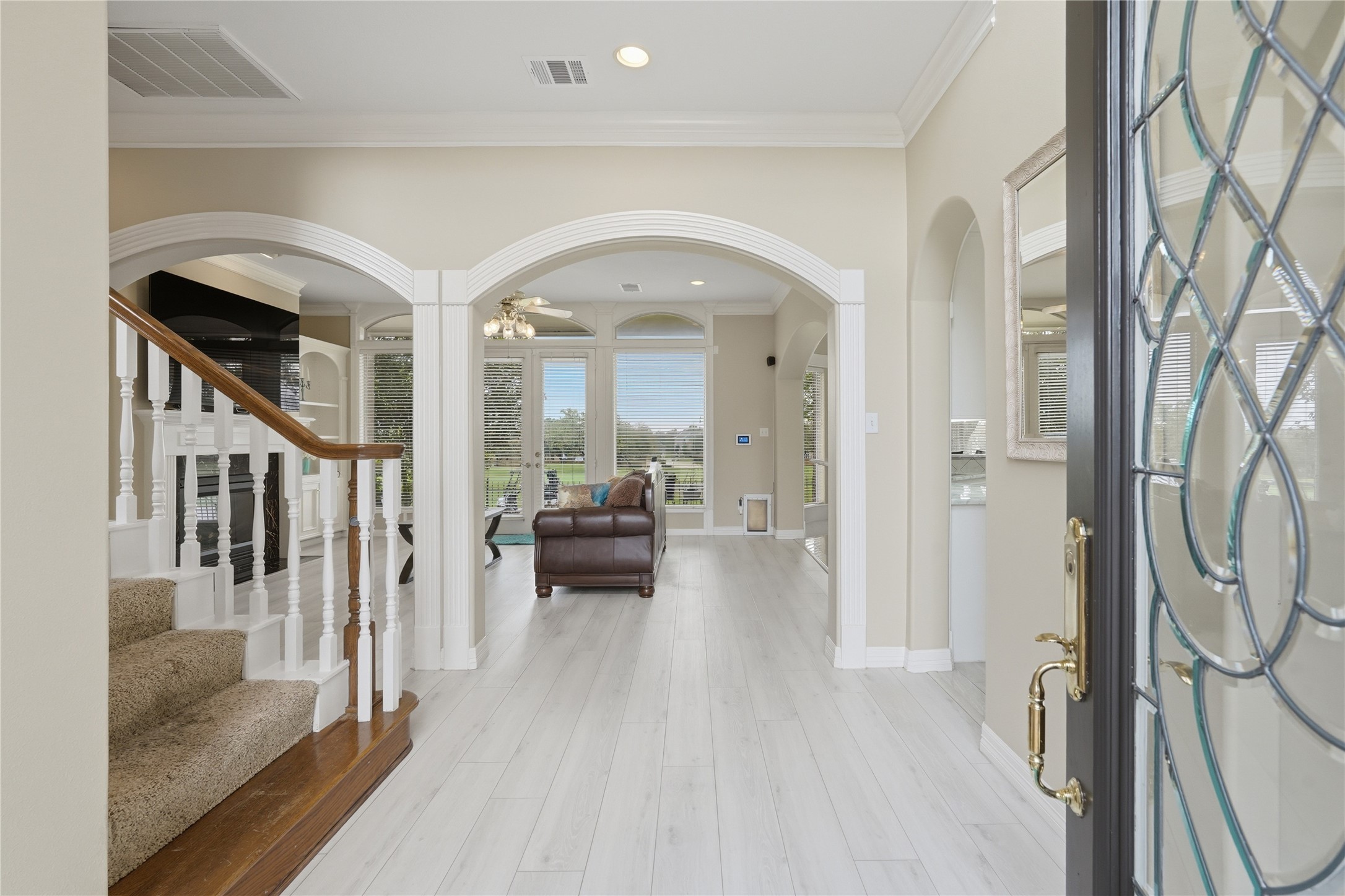 55 Monterrey Road East Montgomery, TX 77356 - Photo 7 of 50 This inviting entryway features elegant archways and light wood flooring, leading to a bright living area with large windows. The staircase offers a classic touch with white spindles and a wooden handrail.