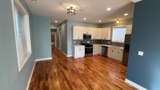22 North Parkside Avenue, Unit 1 Chicago, IL 60644 - Photo 3 of 13 a kitchen with stainless steel appliances granite countertop a refrigerator a stove top oven and a sink with wooden floor