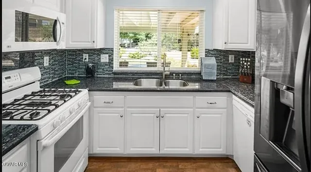 a kitchen with granite countertop a sink cabinets stainless steel appliances and a window