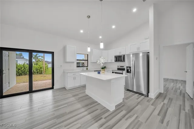 a large white kitchen with a refrigerator a sink dishwasher a stove and white cabinets with wooden floor