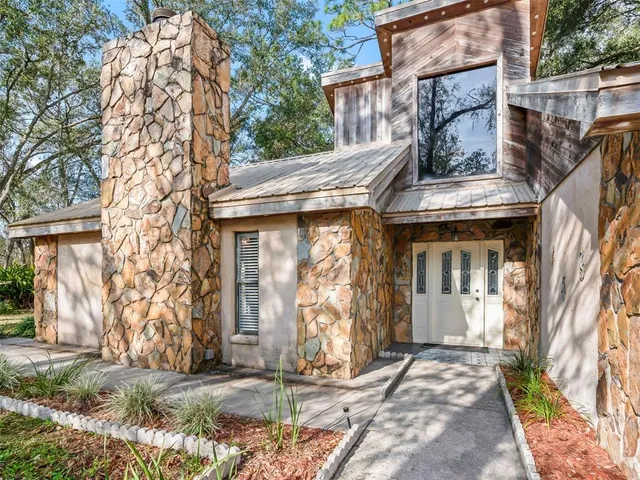 a view of a house with brick walls plants and large tree