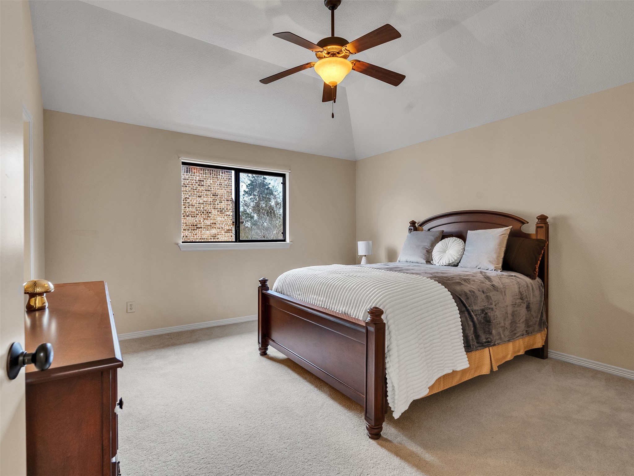 6914 Sandwedge Point Court Spring, TX 77389 - Photo 40 of 50 This bedroom features a vaulted ceiling with a ceiling fan, neutral walls, and carpeted flooring. It includes a window with a view and is furnished with a classic wooden bed and dresser, creating a cozy and inviting space.