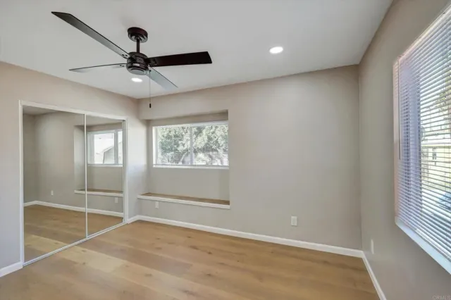 a view of an empty room with wooden floor and a ceiling fan