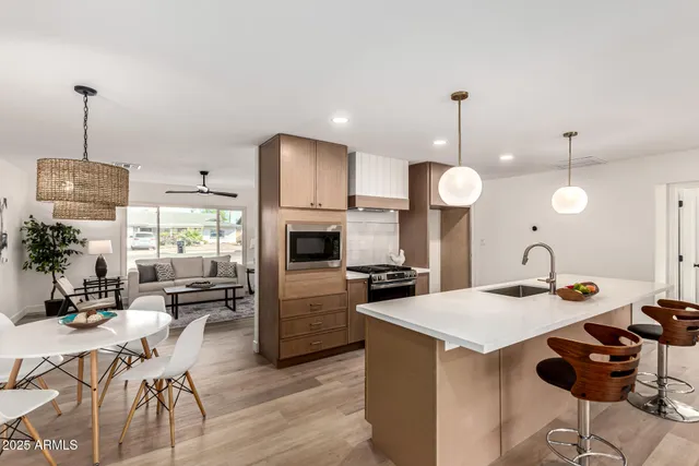 a kitchen with stainless steel appliances kitchen island granite countertop a stove a sink a refrigerator a dining table and chairs with wooden floor
