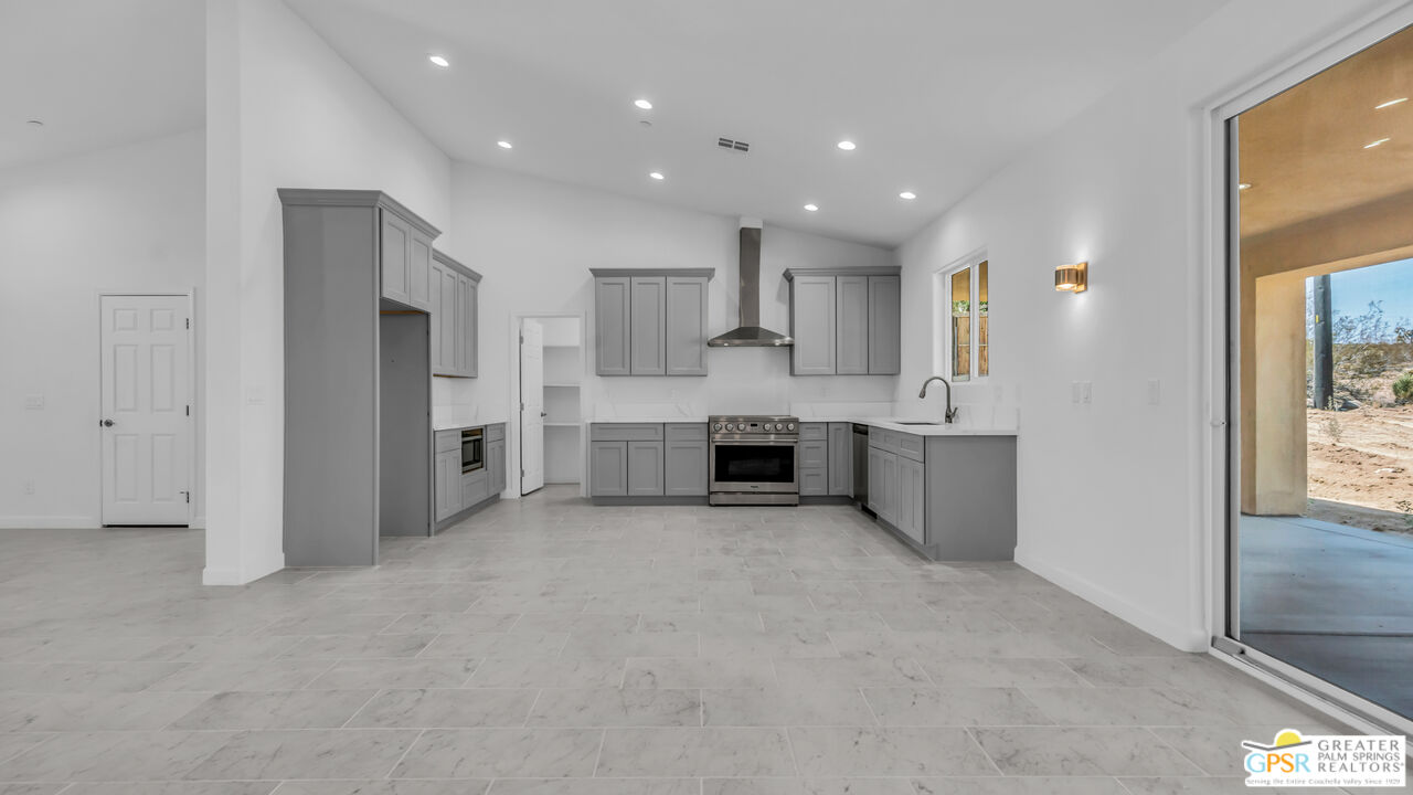 7160 Olympic Road Joshua Tree, CA 92252 - Photo 9 of 58 a large white kitchen with kitchen island a sink a stove a refrigerator and white cabinets