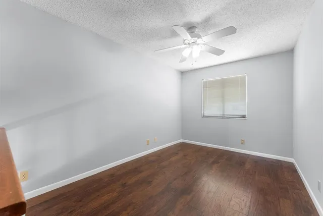 a view of an empty room with wooden floor and a ceiling fan